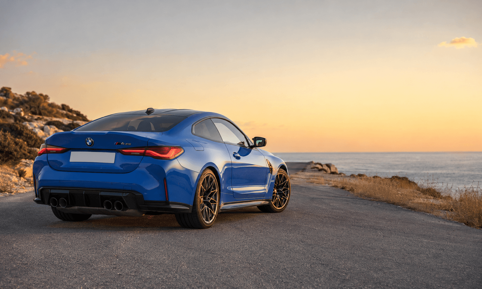 Kuzey Kıbrıs sahil yolunda gün batımında mavi BMW M4 CS arka görünümü